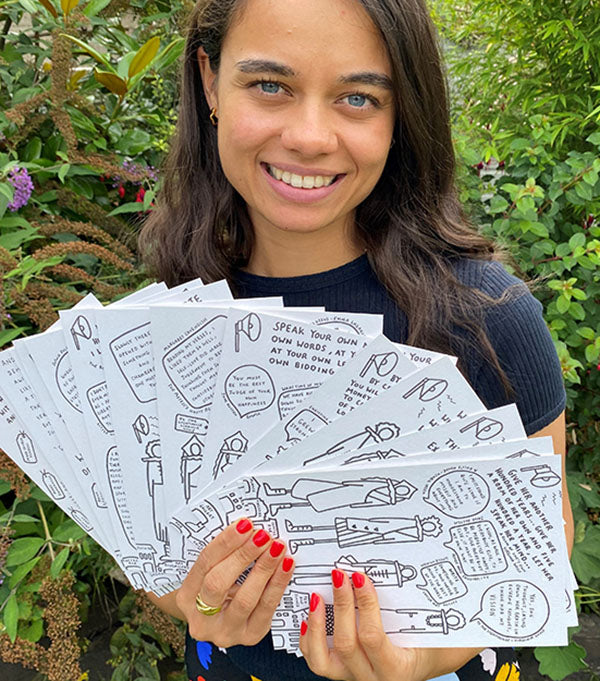a woman holding illustrated cards standing in a garden
