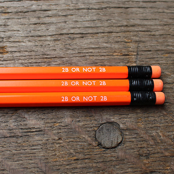 Orange pencils with black ferrules labeled '2B OR NOT 2B' on a wooden surface