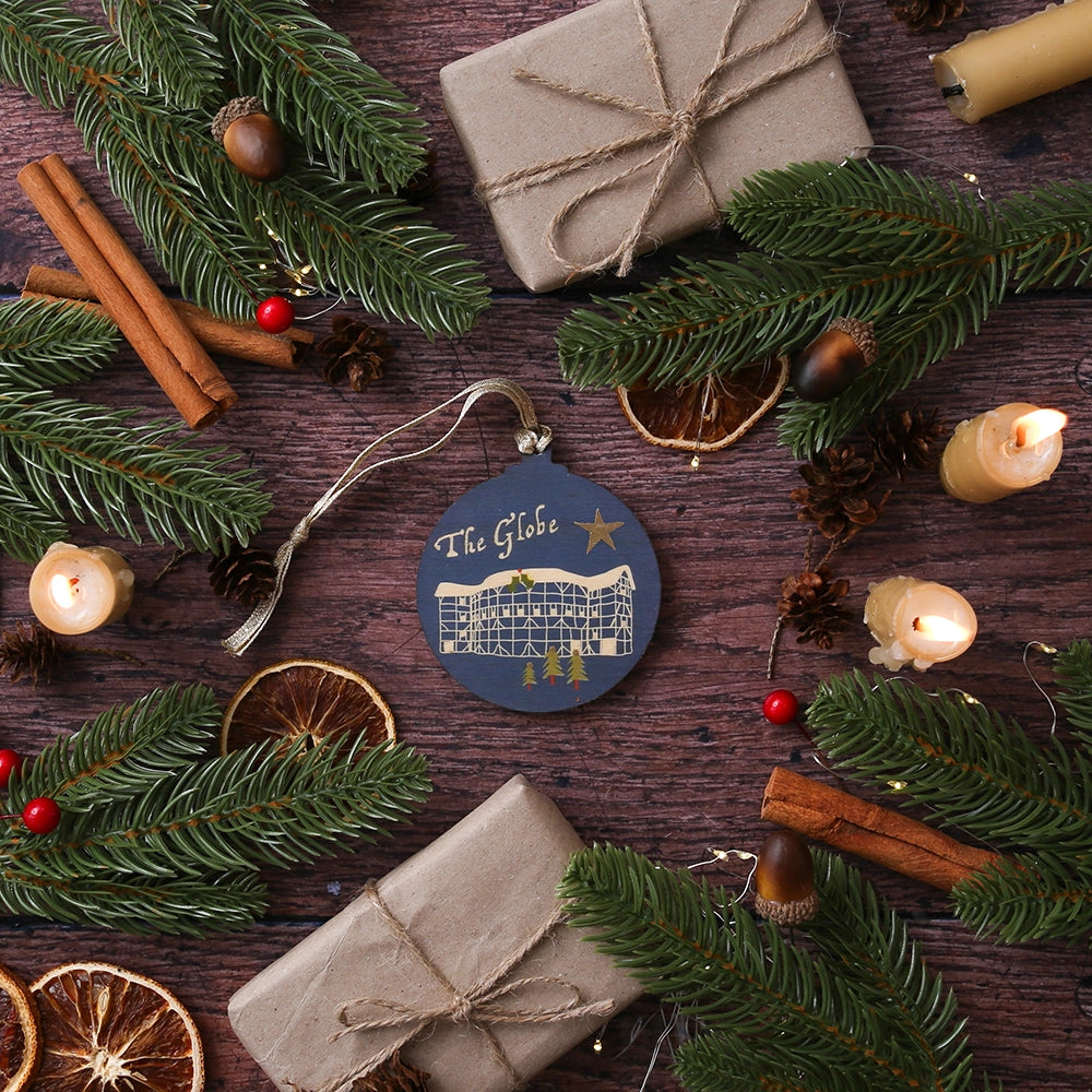 Blue round wooden decoration with 'The Globe' and stylised drawing of the Globe Theatre on wooden background with Christmas greenery