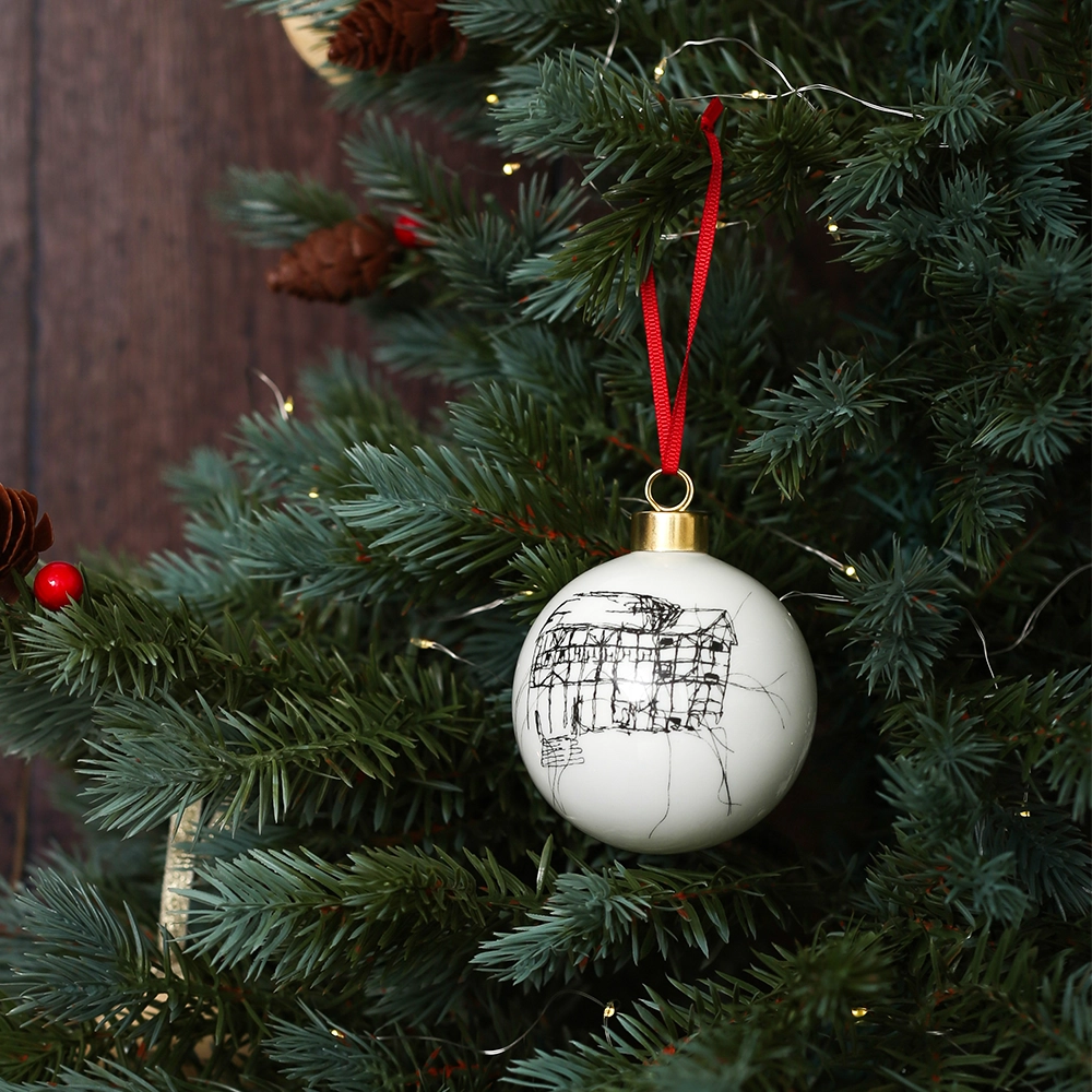 White glass bauble with black etched drawing of Shakespeare's Globe and gold top, with red tied ribbon, on Christmas tree