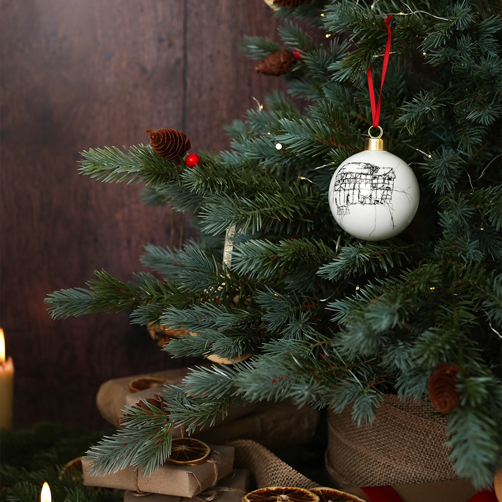 White glass bauble with black etched drawing of Shakespeare's Globe and gold top, with red tied ribbon, on Christmas tree