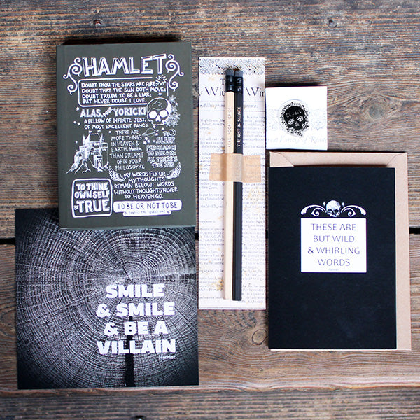 A selection of stationery products including pencils on a backing card, a grey journal with white text, a black and white print, a black greetings card and a black and white pin badge