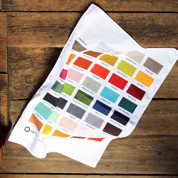 White cotton tea towel, portrait orientation with colour swatches in rows across, 5 per row, on wooden background