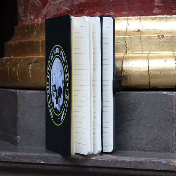 Black matt portrait orientated hardback journal with centre white skull graphic and surrounding text, showing open book, lined pages