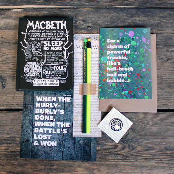 A group of stationery products including, pencils on a backing card, a journal with white print, a green greetings card, a grey print and a black and gold pin badge.