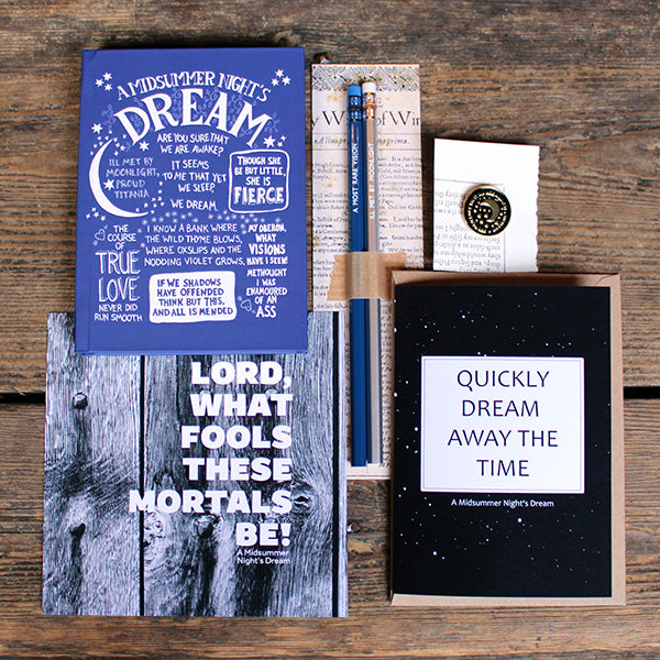 A selection of stationery products including pencils on a backing card, a blue journal with white text, a blue-grey print, a dark blue greeting card and a black and gold pin badge
