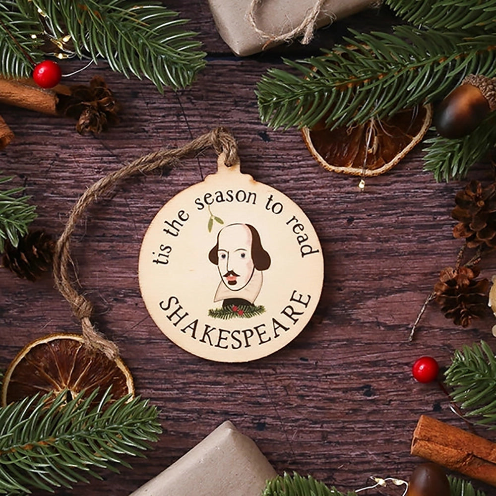 Round, flat, wooden Christmas decoration with Shakespeare's face in centre surrounded by 'tis the season to read' text., on wooden background with Christmas greenery