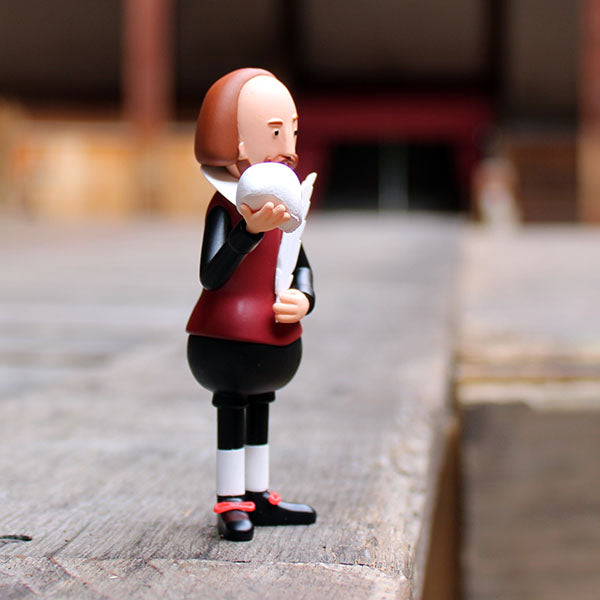 plastic figure of Shakespeare wearing a black and deep red costume holding a white skull and feather