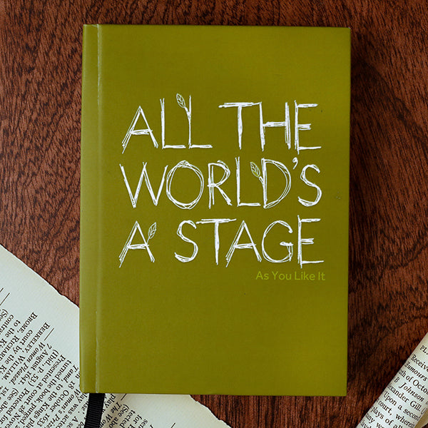 Green book with 'All the World's a Stage' quote on a wooden surface
