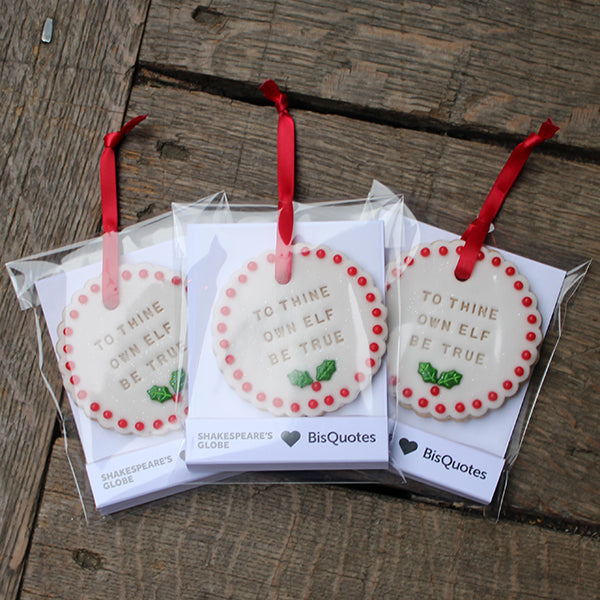 Three decorative Christmas biscuits with text and red ribbons on a wooden surface.