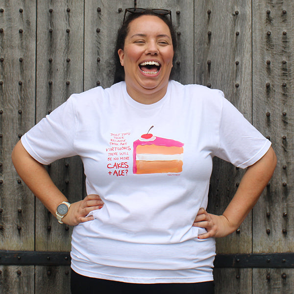 White cotton standard fit t-shirt with centre front graphic of a slice of vanilla cake with hot pink frosting and a cherry on top, with scratchy red writing down the left side, on female model standing in front of wooden doors