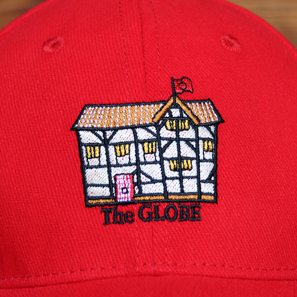 Red cotton baseball cap with curved bill and embroidered cartoon Shakespeare's Globe on front