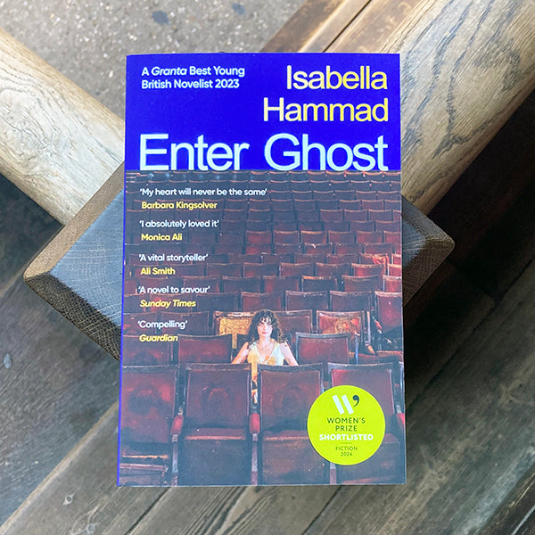 Book cover of 'Enter Ghost' by Isabella Hammad on a wooden surface