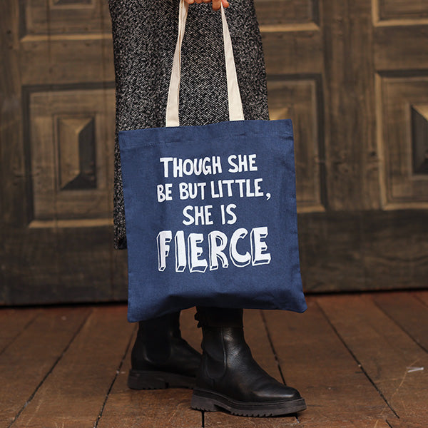 A mid-blue bag with black mid-length handles. The bag has a printed quote from Shakespeare play, A Midsummer Night's Dream (though she be but little, she is fierce.)