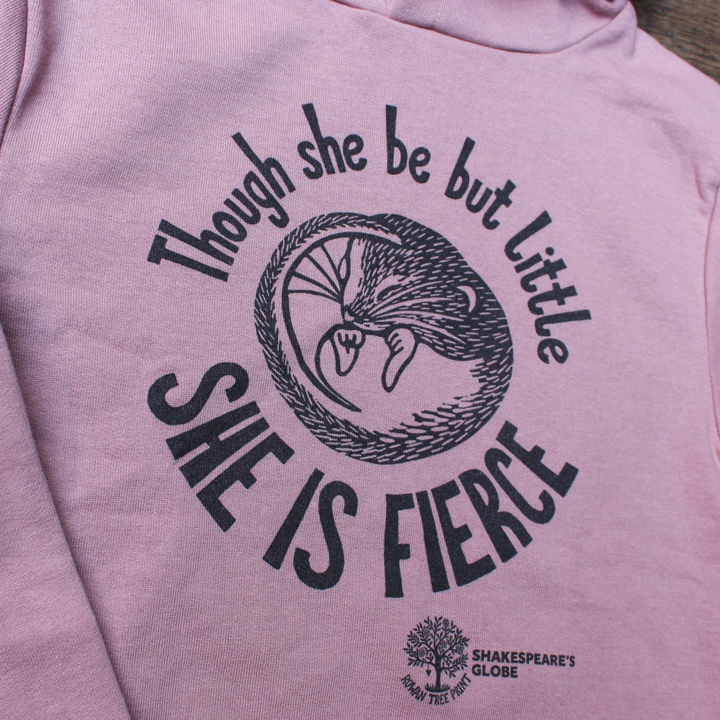 Pink hoodie with 'Though she be but little, she is fierce' text and Shakespeare's Globe logo.