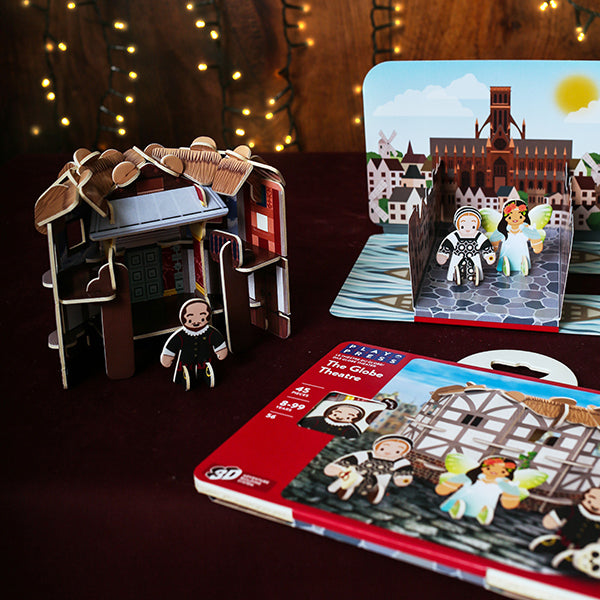 Toy theater set with miniature figures and a book on a wooden surface with string lights in the background.