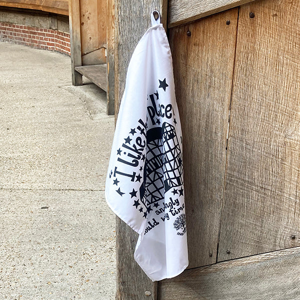 White tea towel with black text and graphics hanging on a wooden post