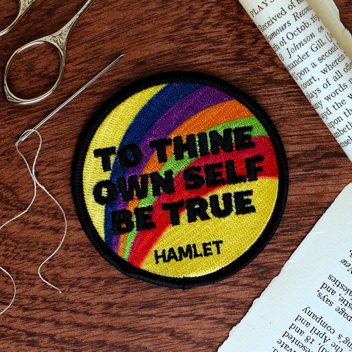 Embroidered patch with rainbow design and text on a wooden surface with sewing tools.