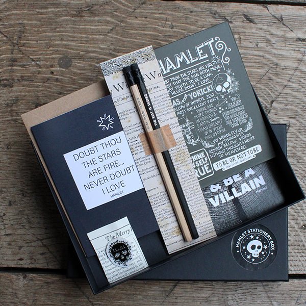 Open black card box with black quote print, black quote card, nude and black pencils with stamped quotes, black quote hardback notebook, and black skull pinbadge