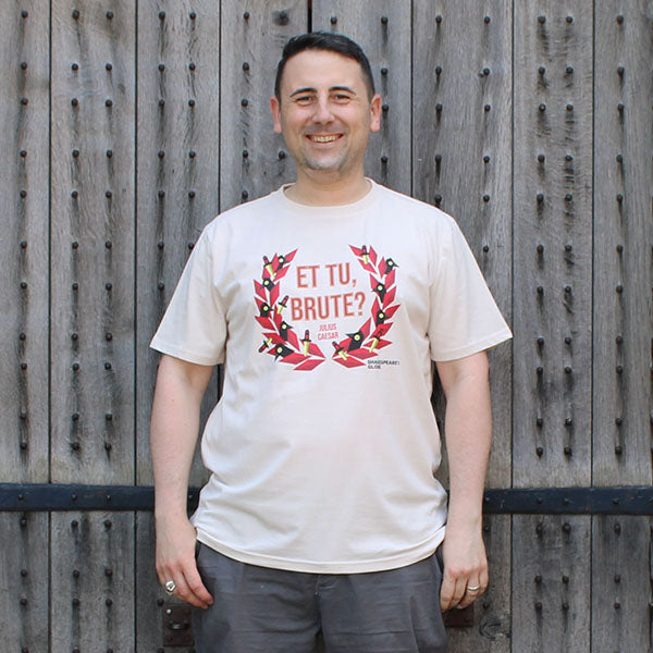 Beige t-shirt with centre front graphic of red laurel wreath with ravens and daggers within it, surrounding red graphic text
