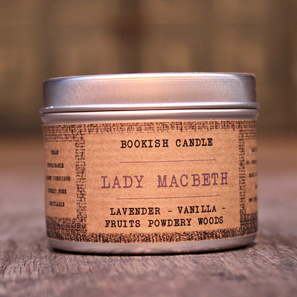 White potted candle in silver tin with tan coloured label surround with old time black print