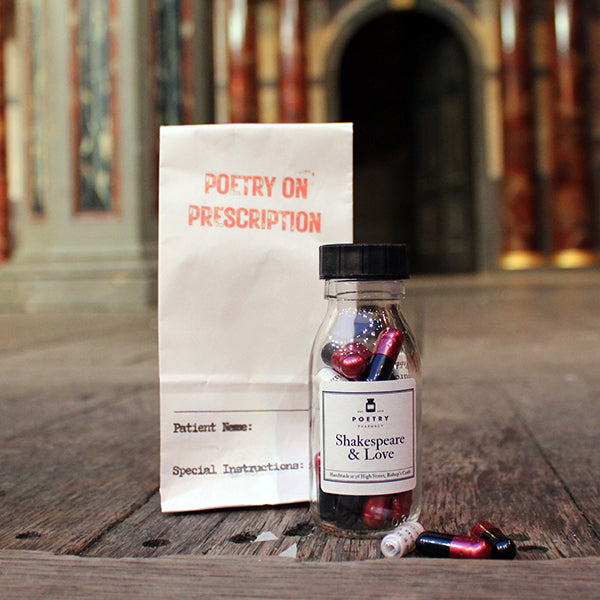 Small glass bottle with white sticker label with black text, filled with white and magenta and black pills, sitting in front of white paper prescription bag