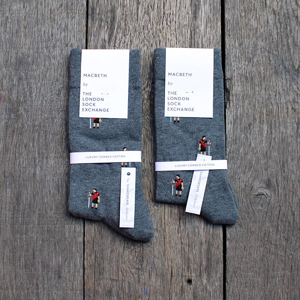 Marled grey cotton blend socks with repeating pattern Macbeth approximately 1 inch apart, with white card packaging