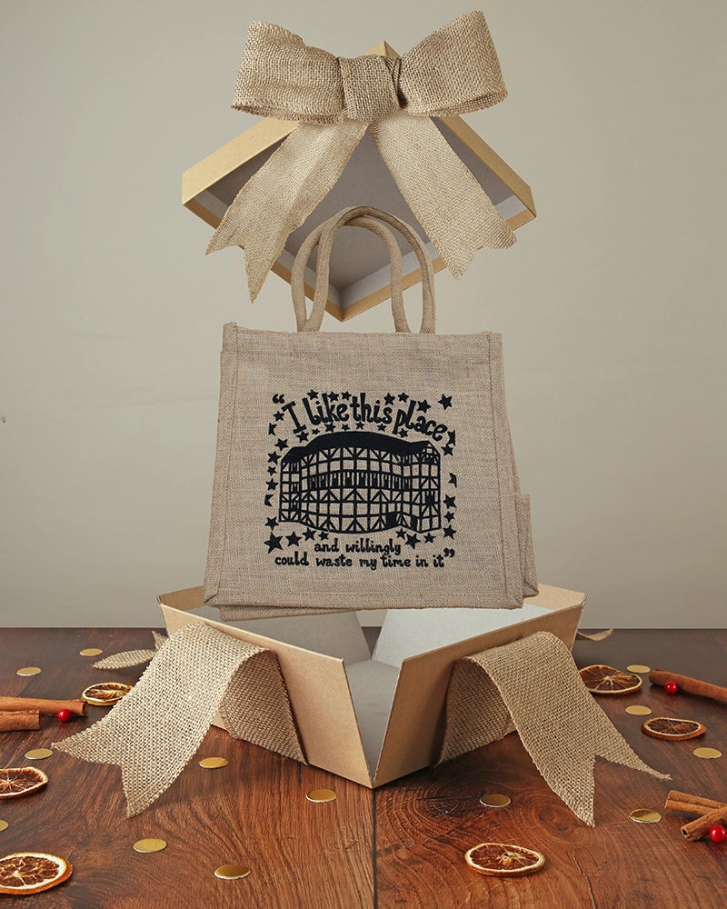 Jute tote bag with black graphic text popping out of a kraft box with hessian bow