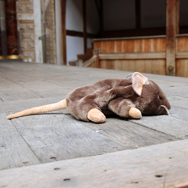 Sandy brown soft toy rat with white whiskers and beige inner ears, feet, nose and tail on wooden stage