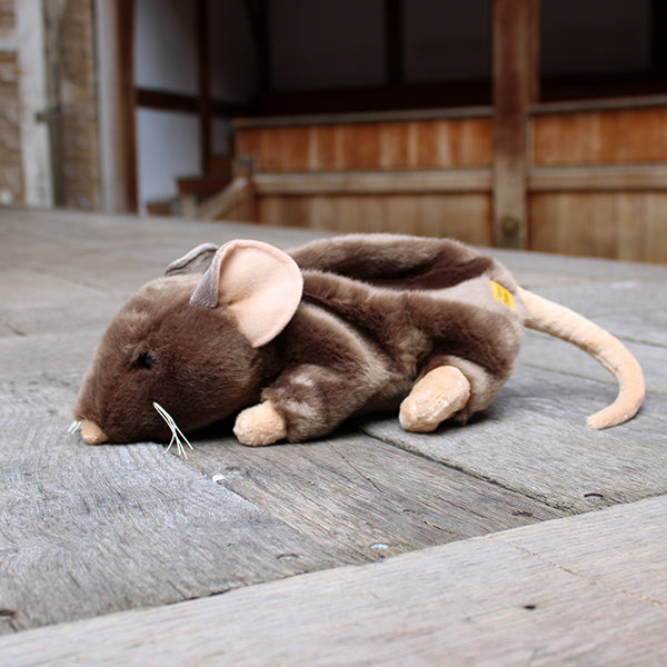 Sandy brown soft toy rat with white whiskers and beige inner ears, feet, nose and tail on wooden stage