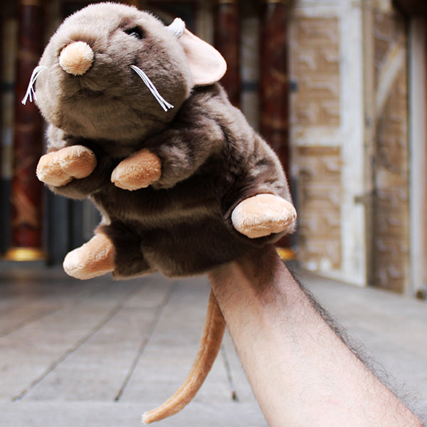 Sandy brown soft toy rat with white whiskers and beige inner ears, feet, nose and tail on wooden stage