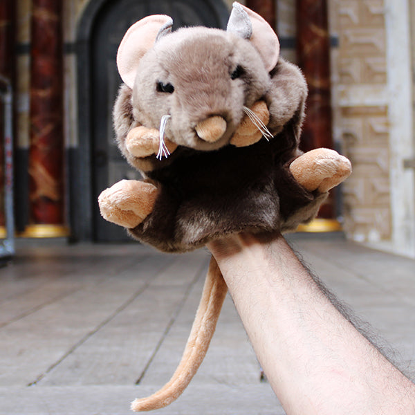 Sandy brown soft toy rat with white whiskers and beige inner ears, feet, nose and tail on wooden stage