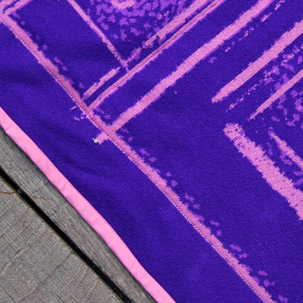 Closeup of fabric texture of deep purple banner with pink graphics, bound with pink edging