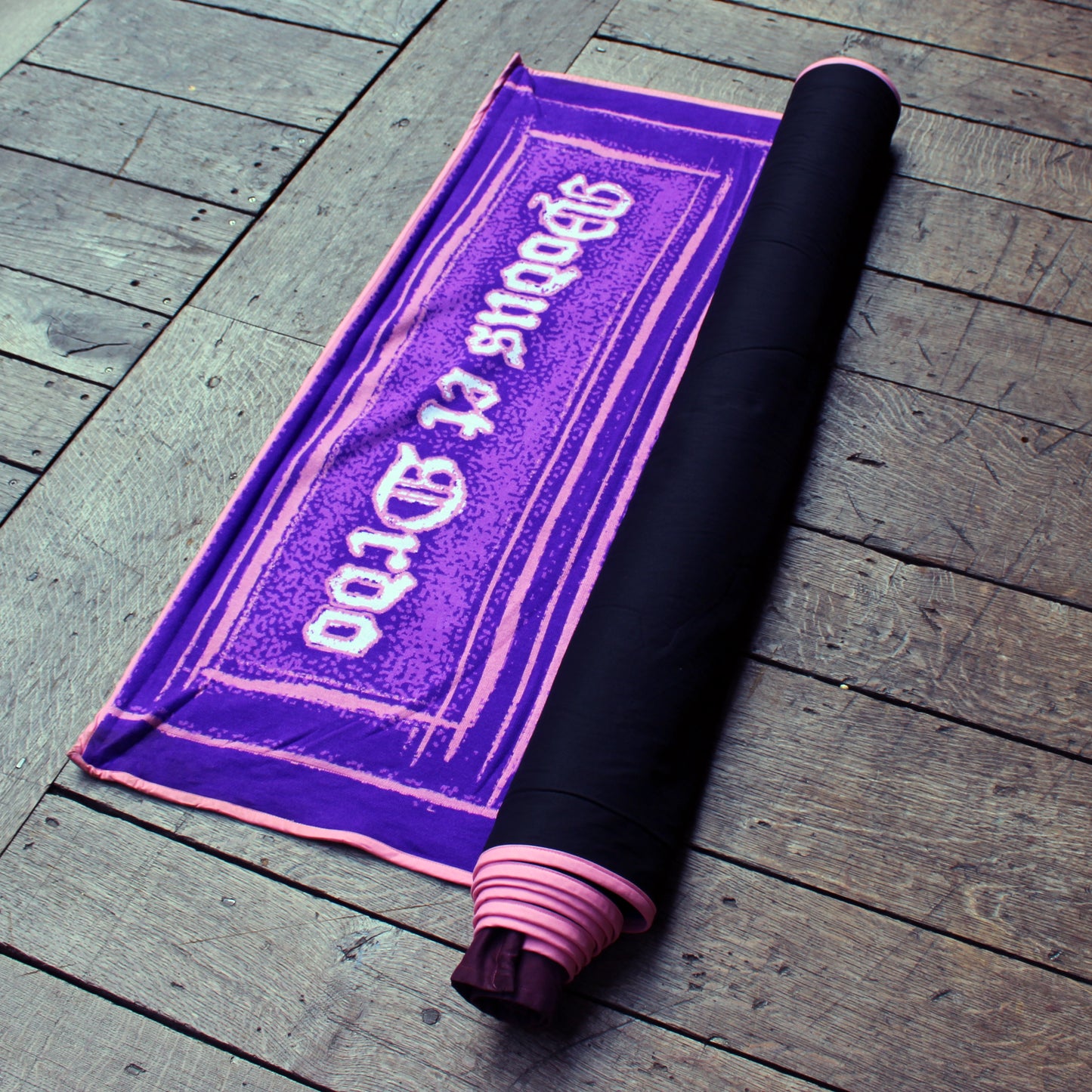 Deep purple fabric banner, with pink and white graphic and black fabric backing, rolled on wooden stage
