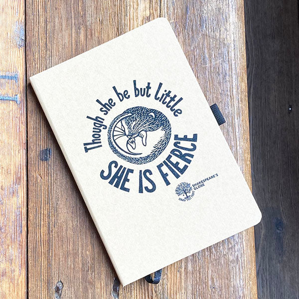 Notebook with 'Though she be but little, she is fierce' quote on a wooden surface
