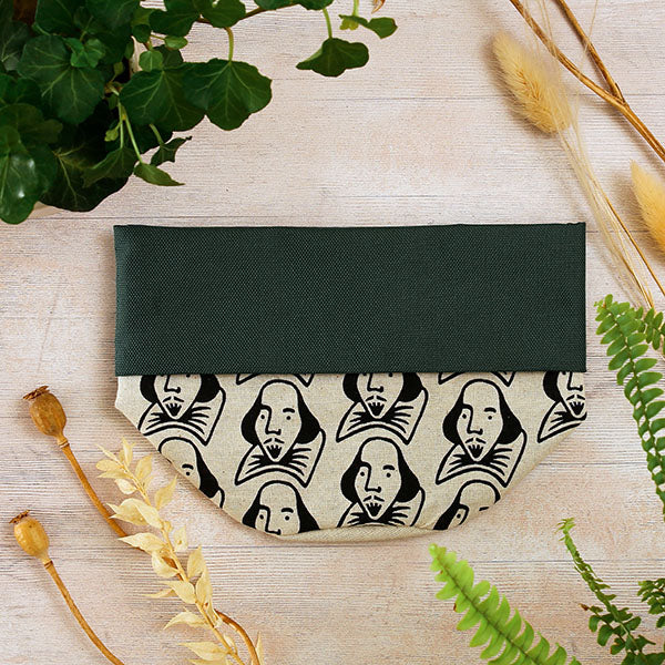 Green storage pot with black and white pattern on a light wooden surface with plants.