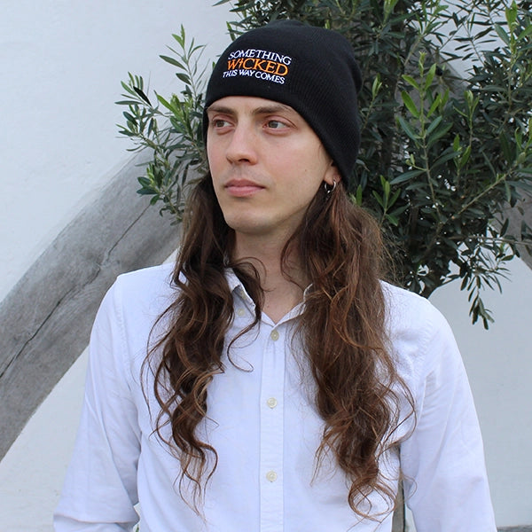 Black beanie hat with an embroidered quote on the front from Shakespeare play, Macbeth in white and orange writing