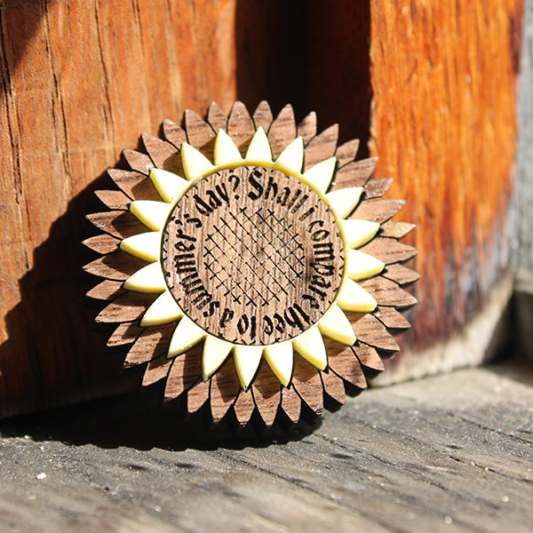 walnut wood and cream acrylic brooch in the shape of a stylised flower with text engraved around the centre