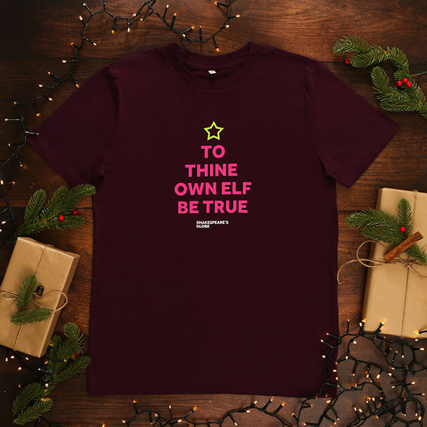 Purple t-shirt with pink text on a wooden surface with Christmas decorations