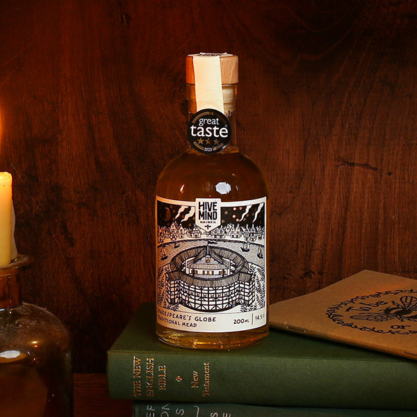 Bottle of 'Hive Mind' mead on books with a candle and coaster in the background