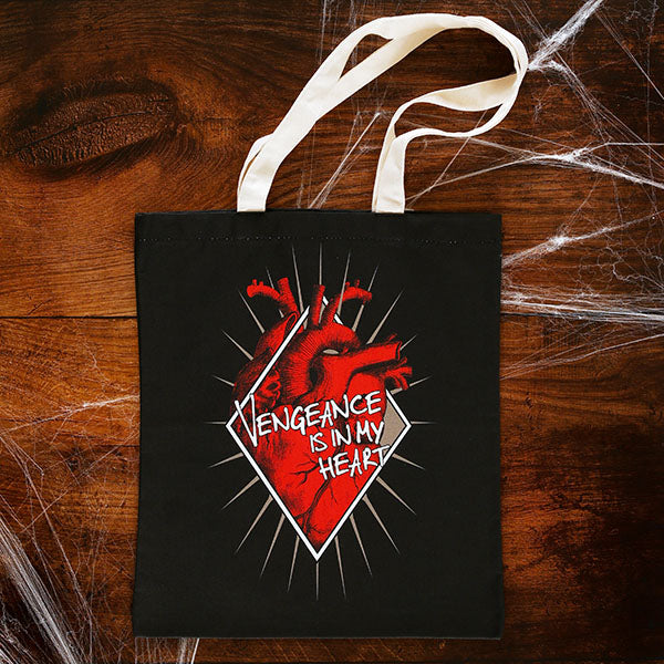 Black cotton bag with natural cotton handles, printed with an image celebrating Shakespeare play, Titus Andronicus. A red anatomical heart is partly enclosed by a white diamond frame. Gold rays emanate from behind the frame. Across the front of the image is a quote from the play (vengeance is in my heart) in white lettering.