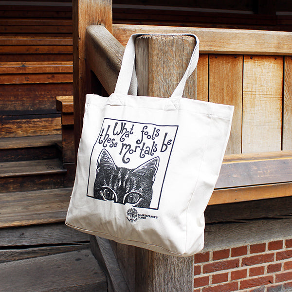 White tote bag with a cat illustration and text hanging on a wooden post.