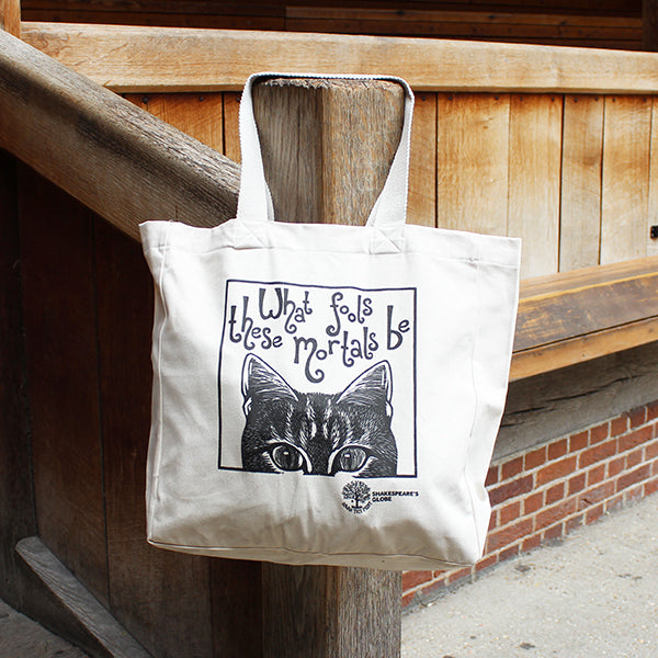 Tote bag with a cat illustration and text hanging on a wooden post.