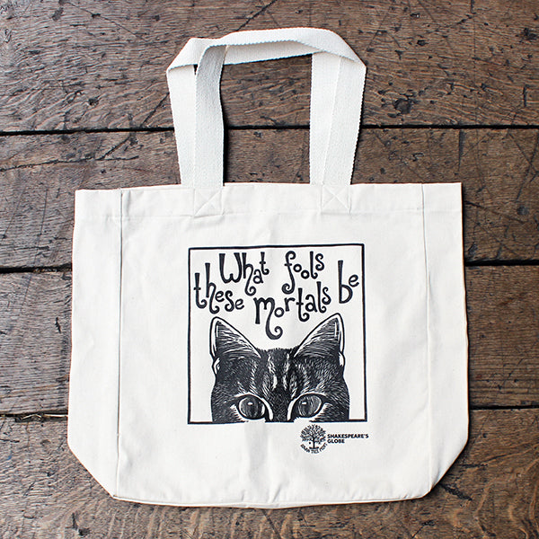 White tote bag with a black cat illustration and text on a wooden surface