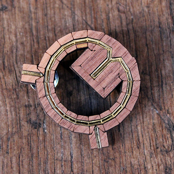 wooden brooch shaped like the Globe Theatre from above. The brooch has the roof line picked out in shiny gold acrylic.