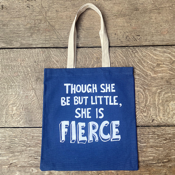 A mid-blue bag with black mid-length handles. The bag has a printed quote from Shakespeare play, A Midsummer Night's Dream (though she be but little, she is fierce.) The quote is printed in white and is made from hand-drawn capital letters