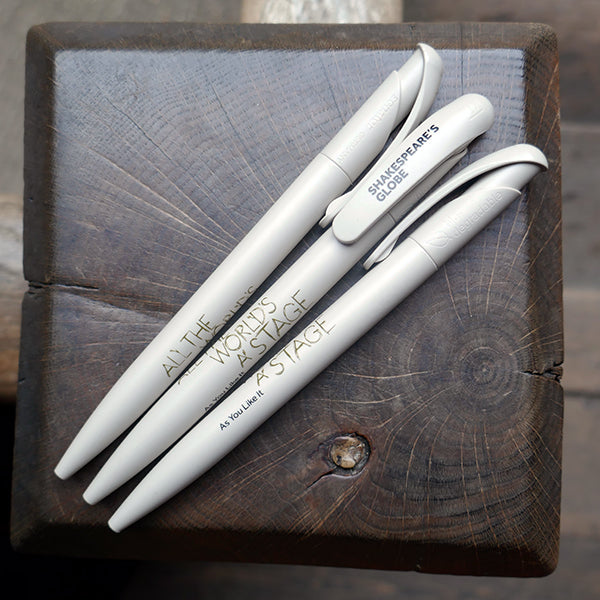Light grey bioplastic ballpoint pen printed on the barrel with a quote from Shakespeare play, As You Like It, "All the world's a stage" in sage green hand-drawn lettering