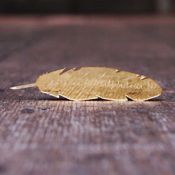 Gold mirrored acrylic brooch in the shape of a feather quill, engraved with a quote from Hamlet