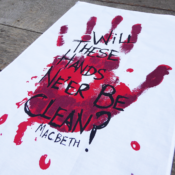White cotton tea towel printed with a large bloody hand-print in reds. Over the hand-print, printed in black is a quote from Shakespeare play, Macbeth (Will these hands ne'er be clean?) The lettering is in an angry, hand-drawn style.