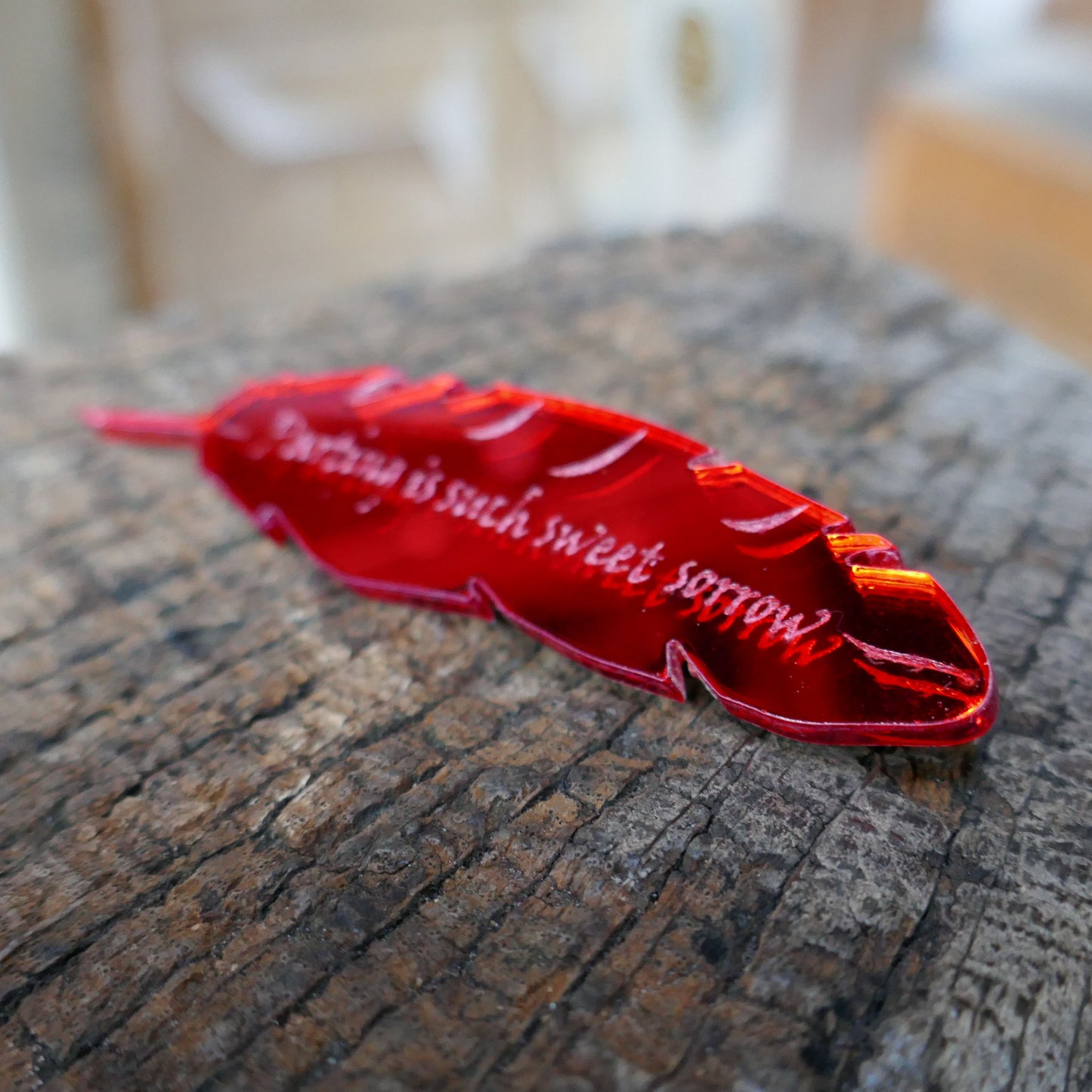 Red mirrored acrylic brooch shaped like a quill and engraved with a quote from Romeo and Juliet